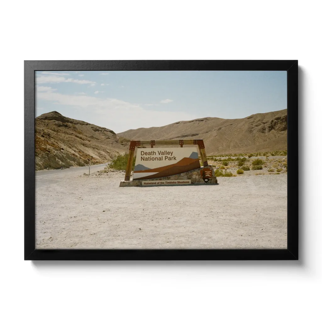 Bildaufnahme eines Schotterparkplatzes, mit dem Einfahrtsschild zum Death Valley National Park