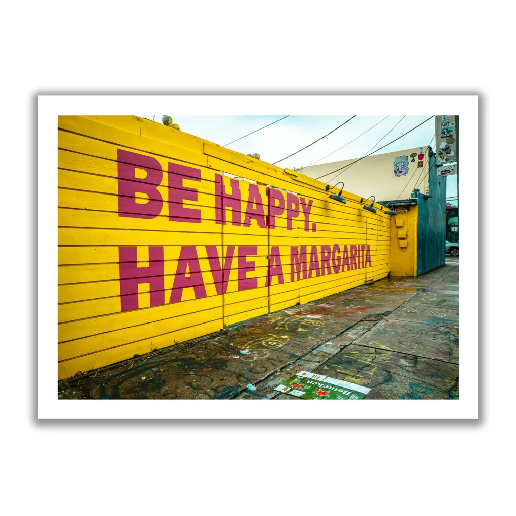 Bildaufnahme von einer gelben Wand mit dem Schriftzug "Be Happy Have a Margarita"