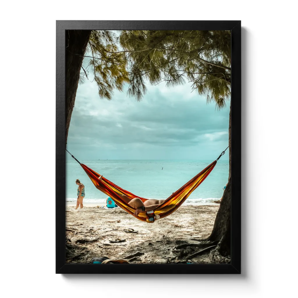 Bildaufnahme eines Mannes, der am Strand unter Palmen in einer Hängematte liegt und das Meer im Hintergrund ist. Das lustige dabei, man sieht sein kleines Bäuchlein.