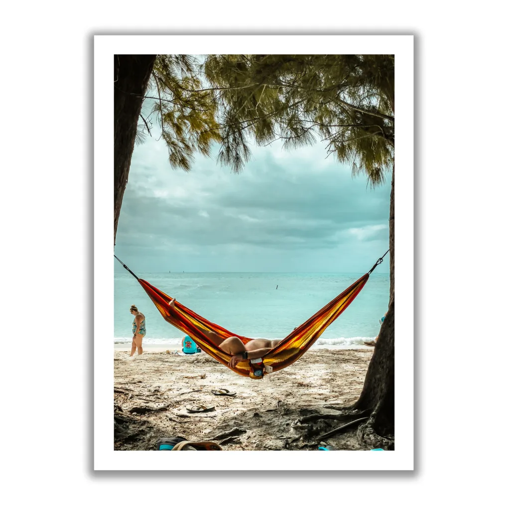 Bildaufnahme eines Mannes, der am Strand unter Palmen in einer Hängematte liegt und das Meer im Hintergrund ist. Das lustige dabei, man sieht sein kleines Bäuchlein.