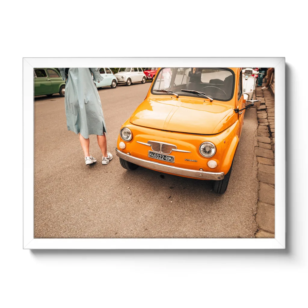 Bildaufnahme eines typischen Oldtimer Fiat in Italien. Das Auto ist knallig orange und neben an steht ein Frau in einem Kleid.