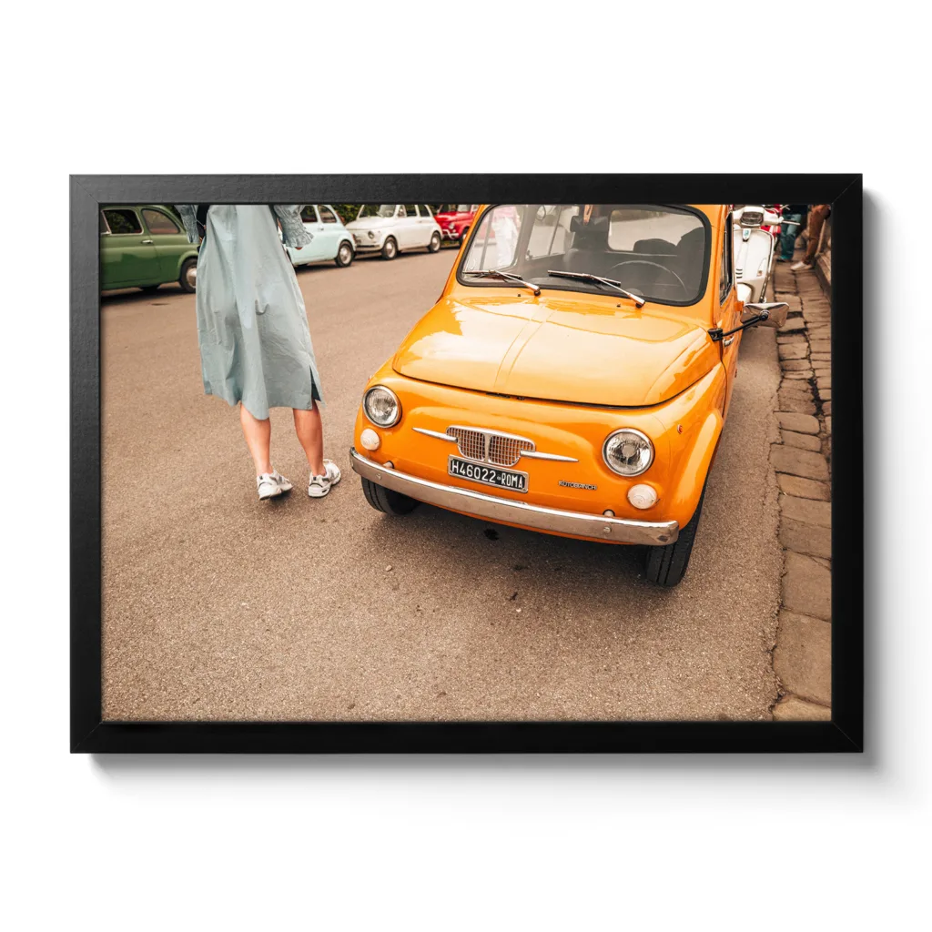 Bildaufnahme eines typischen Oldtimer Fiat in Italien. Das Auto ist knallig orange und neben an steht ein Frau in einem Kleid.