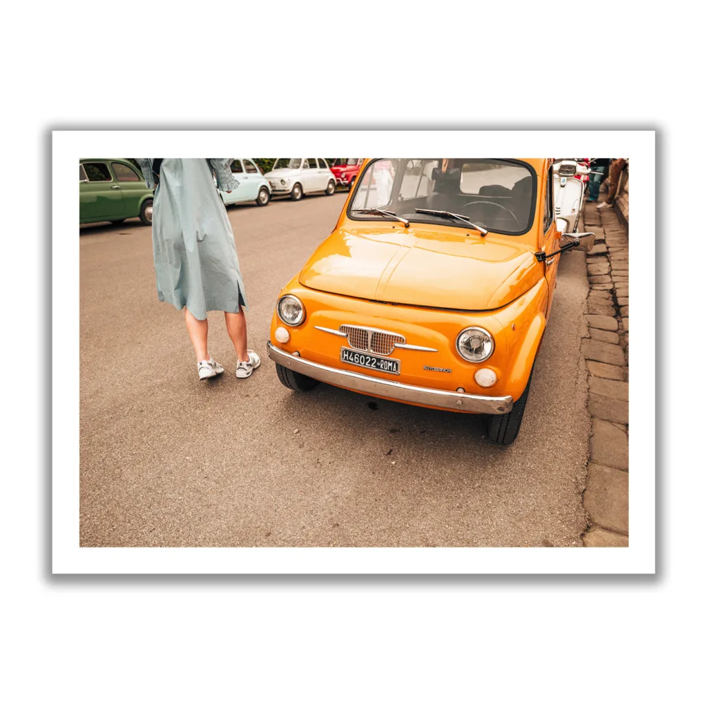 Bildaufnahme eines typischen Oldtimer Fiat in Italien. Das Auto ist knallig orange und neben an steht ein Frau in einem Kleid.